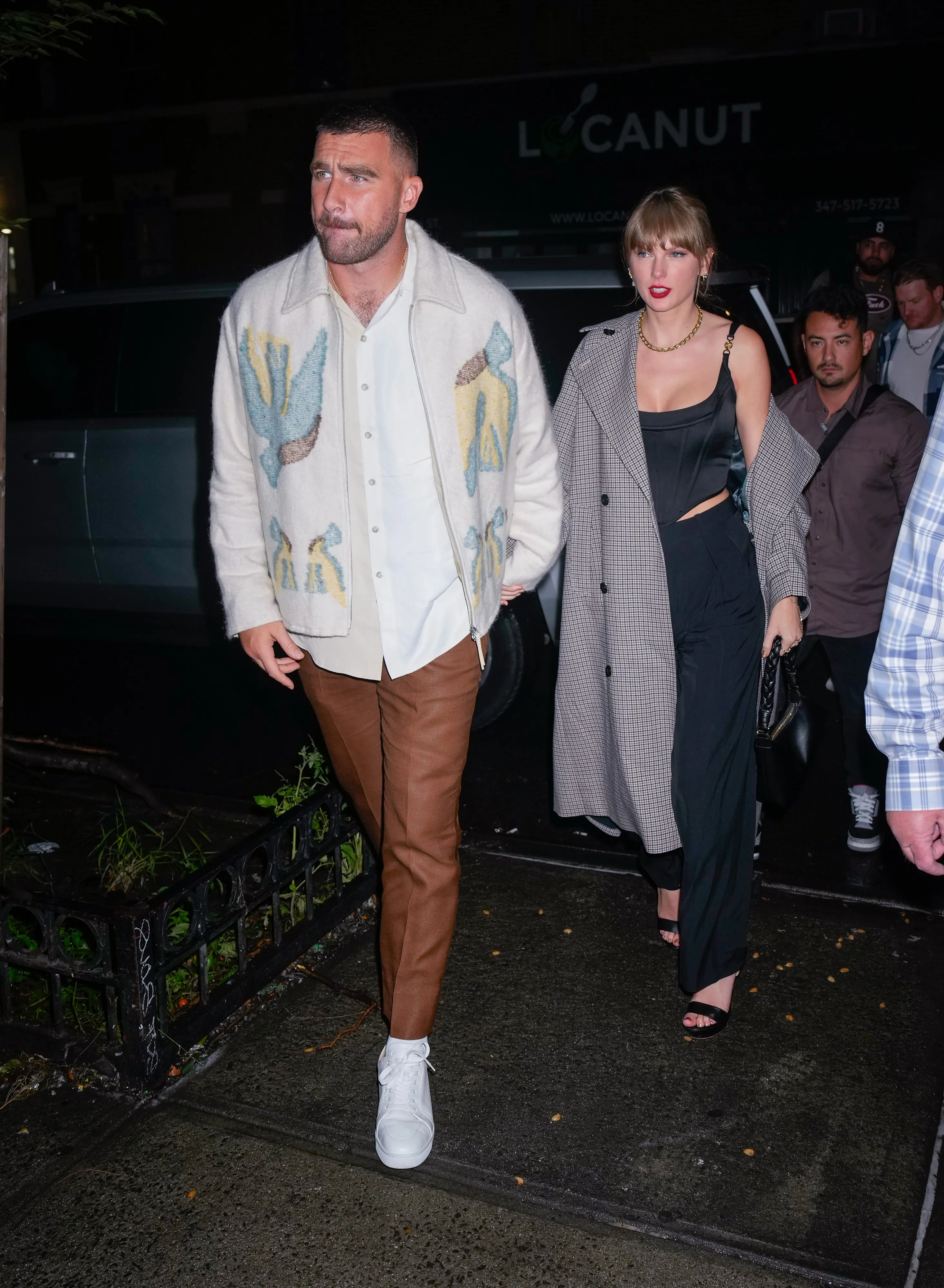 Taylor Swift and Travis Kelce walking together at night.