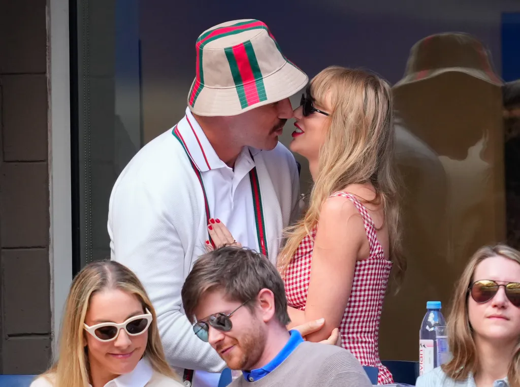 Travis Kelce and Taylor Swift lean in to kiss, while others sit below them.