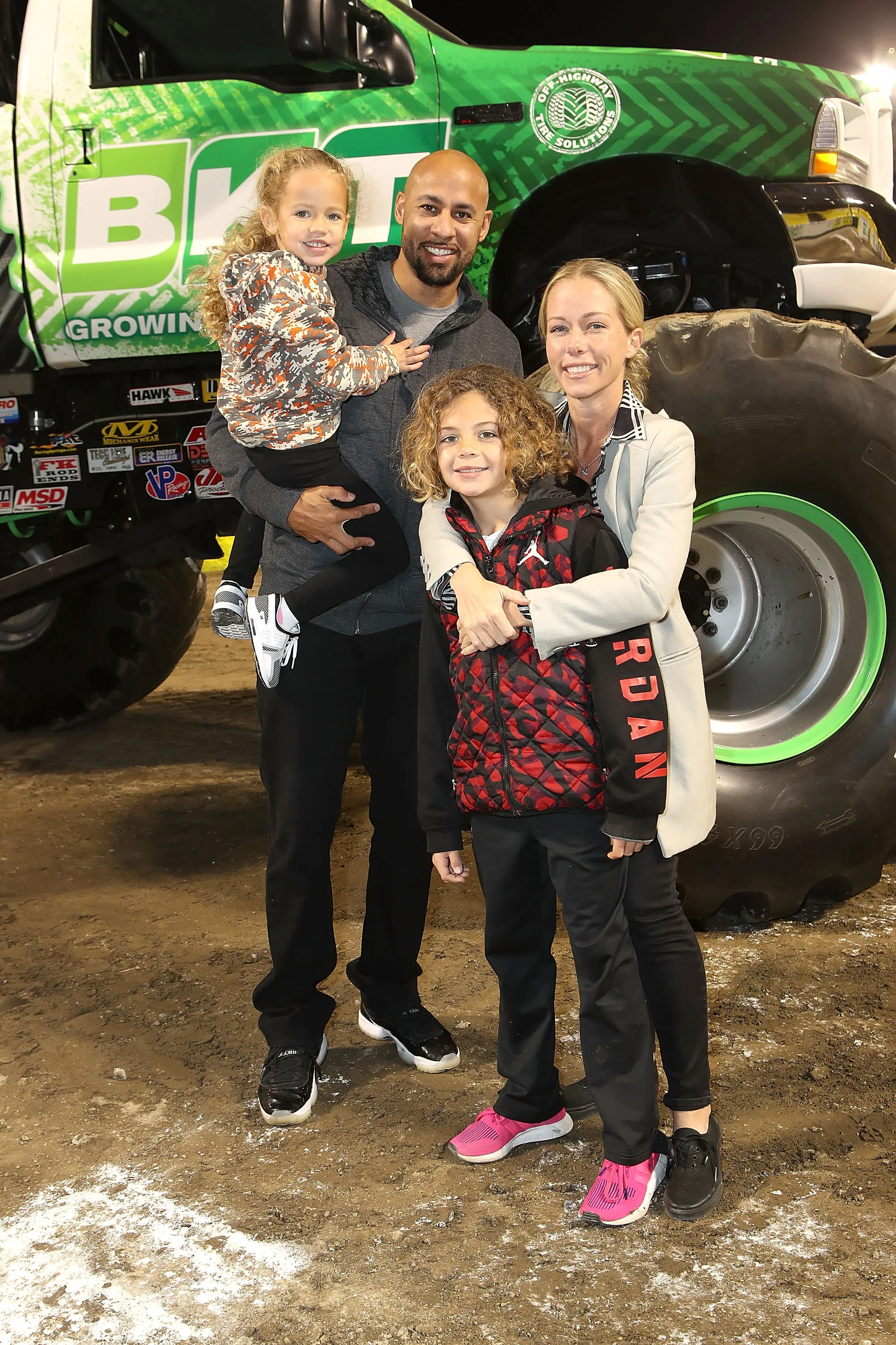 Hank Baskett, Kendra Wilkinson Baskett, and their two children pose in front of a Monster Jam truck.