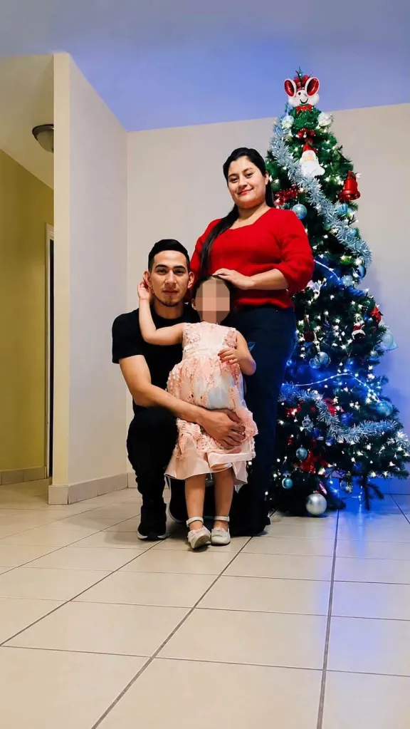Two adults and a child posing in front of a Christmas tree.