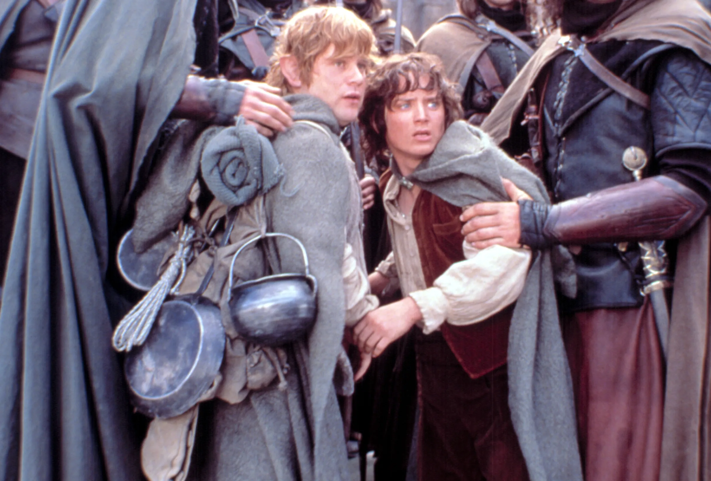 Samwise Gamgee and Frodo Baggins, looking fearful, are captured and held by two men in armor.