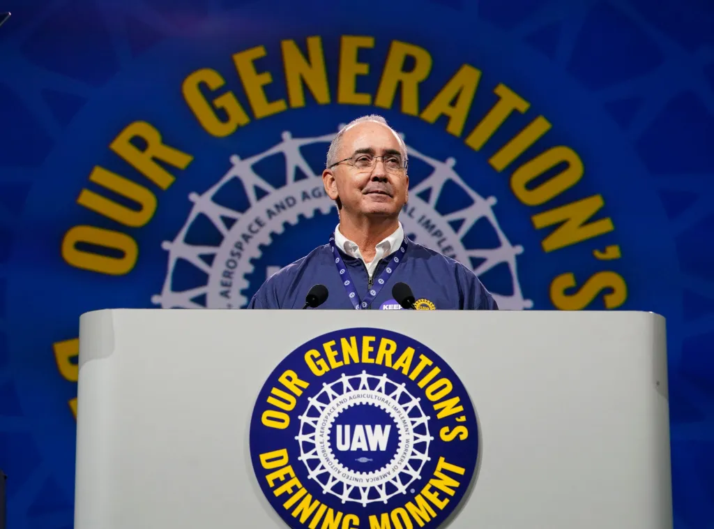 UAW President Shawn Fain speaks at a podium with the UAW logo and 