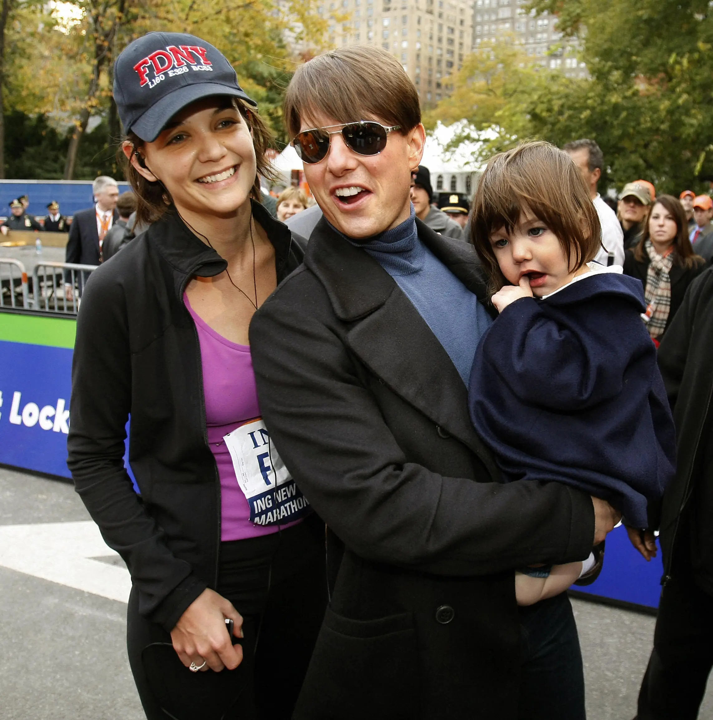 Tom Cruise holding his daughter Suri, with Katie Holmes standing next to them at the finish line of the New York City Marathon.