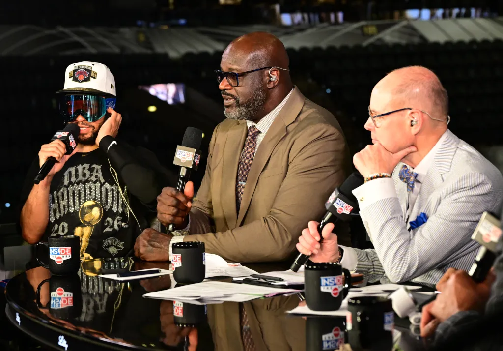Jalen Brunson in an NBA champions hat and blue-tinted goggles is interviewed by Shaquille O'Neal and another commentator.