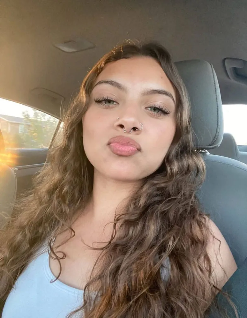 Esmeralda Marcela Gutierrez, a young woman with long wavy brown hair, poses for a selfie inside a car.