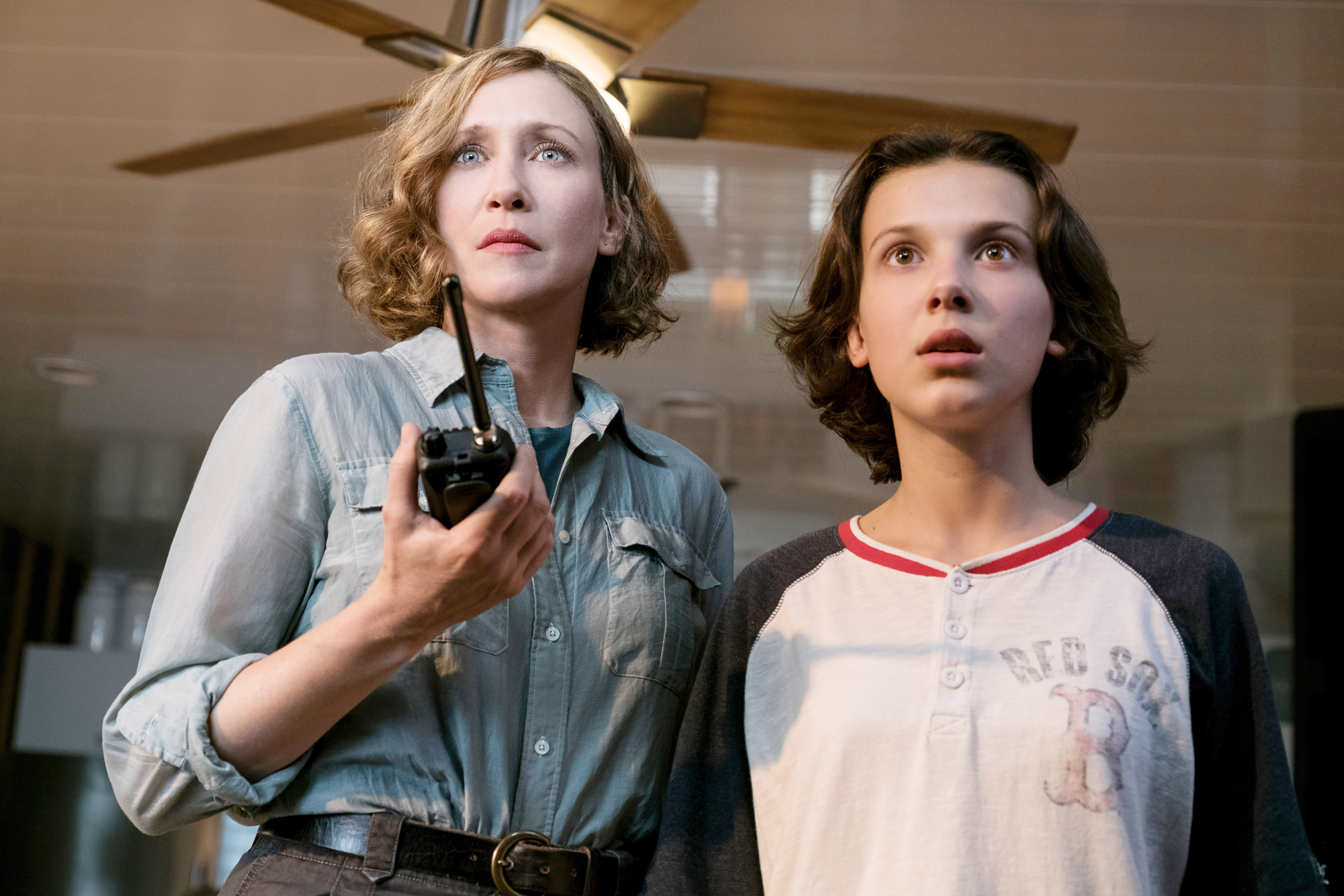 Vera Farmiga holding a walkie-talkie and Millie Bobby Brown looking up.