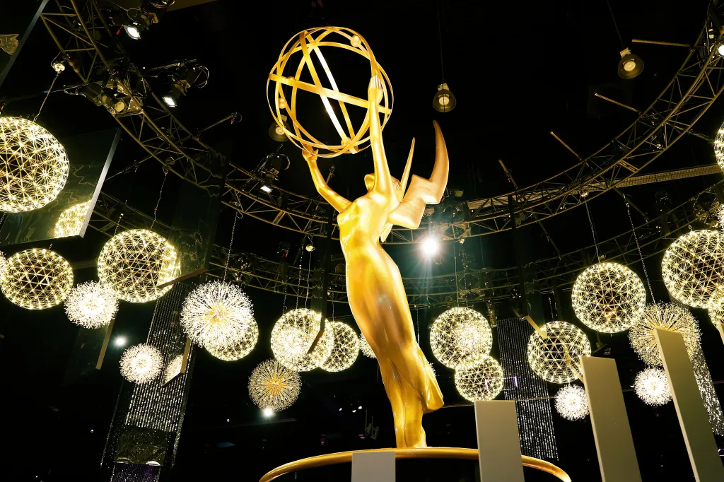 A golden Emmy statue with wings and a globe, surrounded by sparkling spherical lights, is viewed from below at the 77th Primetime Emmys Press Preview.