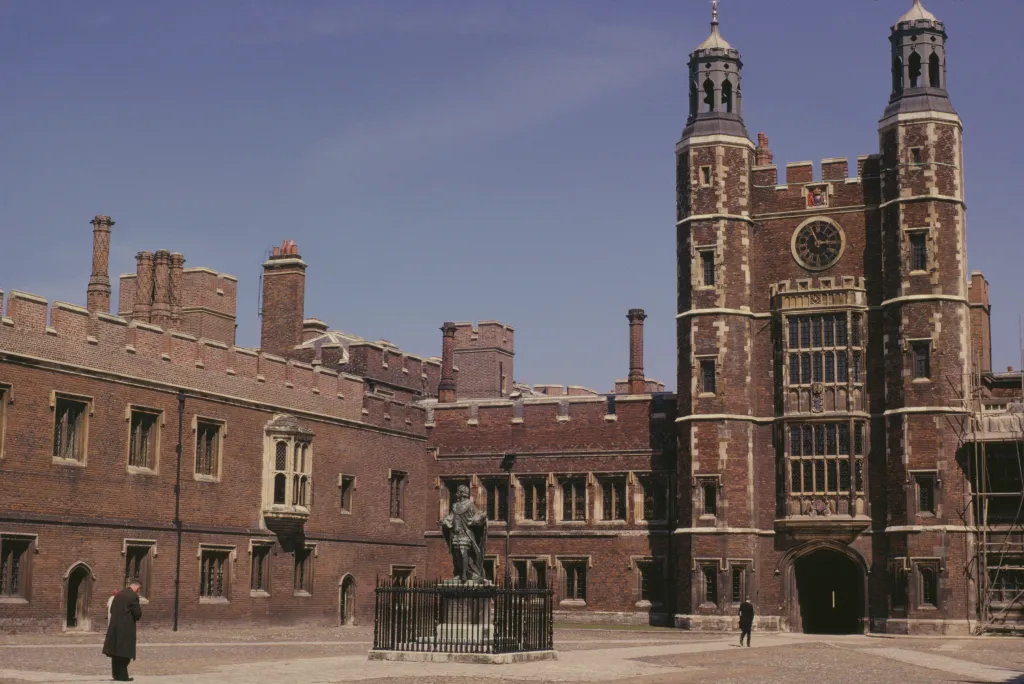 Eton College courtyard with a statue, clock tower, and two men.