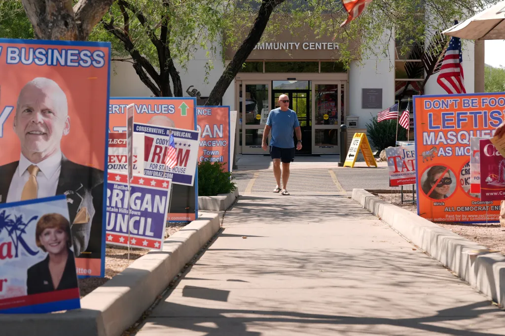A man walking away from a polling site flanked by various election signs in Fountain Hills, Arizona.
