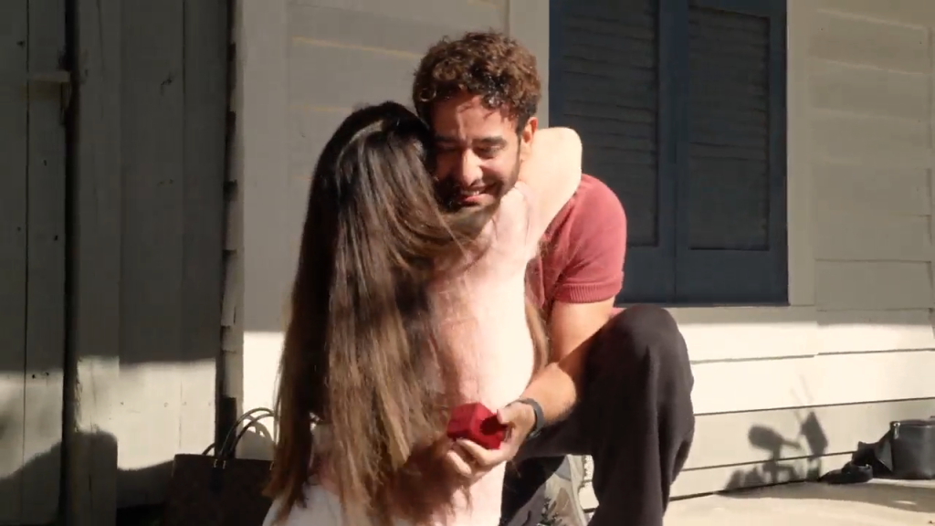 A man kneeling with a ring box embraces a woman.