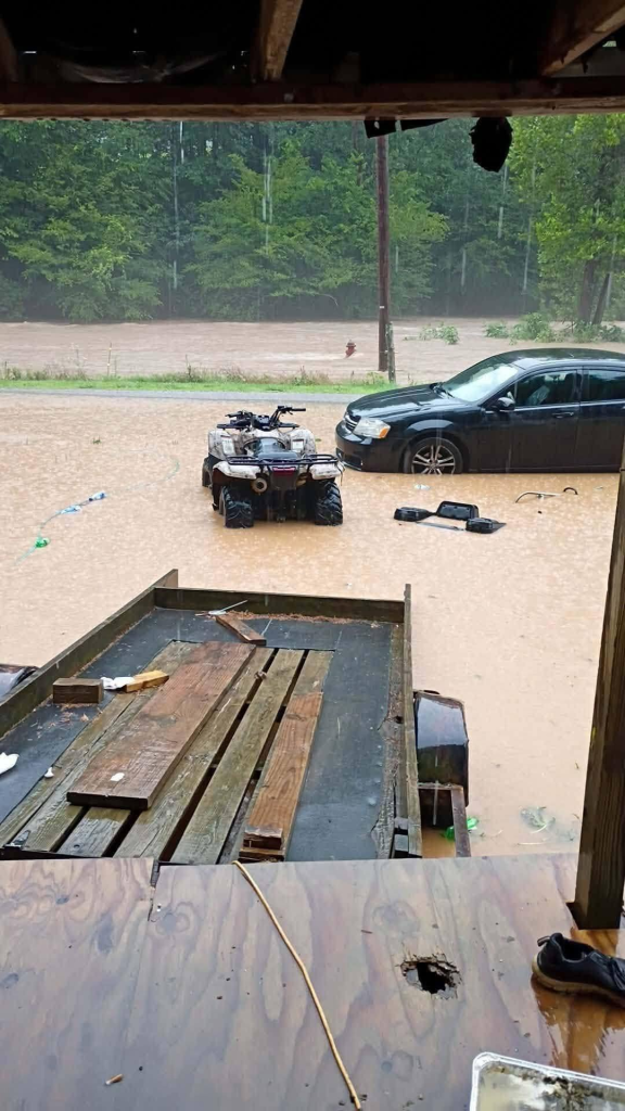 A black car and an ATV sit partially submerged in floodwaters in Wayne County, Kentucky.