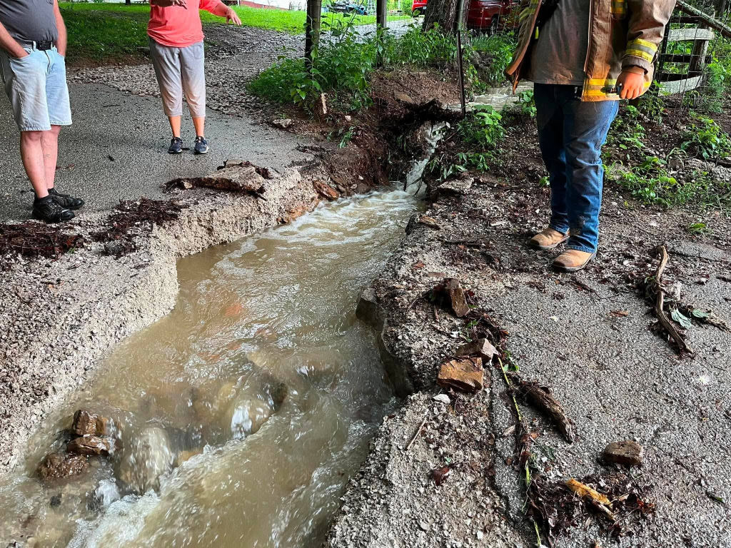 Flooding in Wayne County, Kentucky, showing a washed-out road and rushing water.