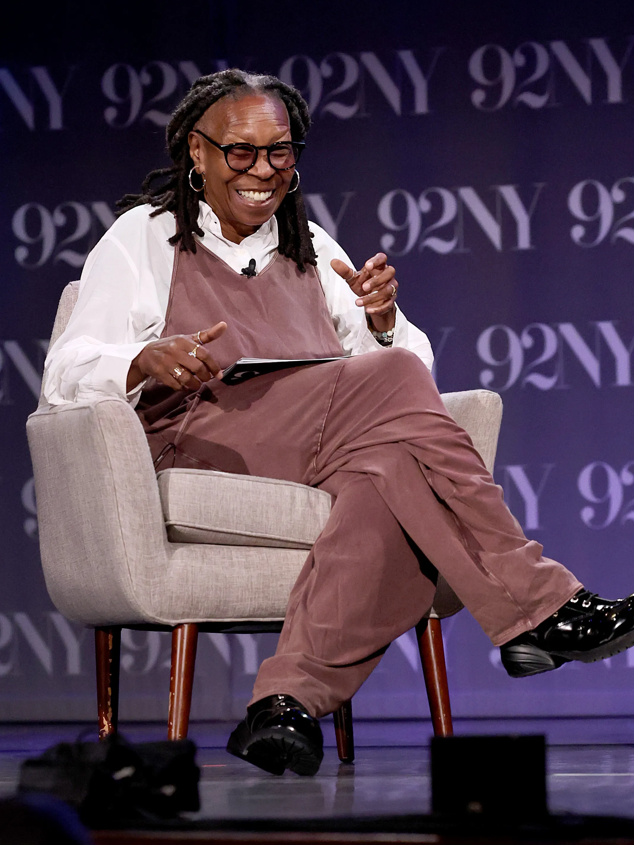 Whoopi Goldberg seated and laughing during an event.