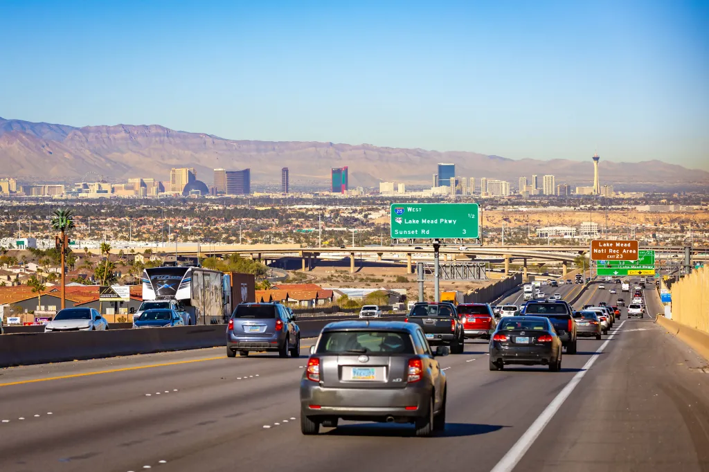 Wide highway view of the Las Vegas city skyline with modern skyscrapers under bright sunlight.