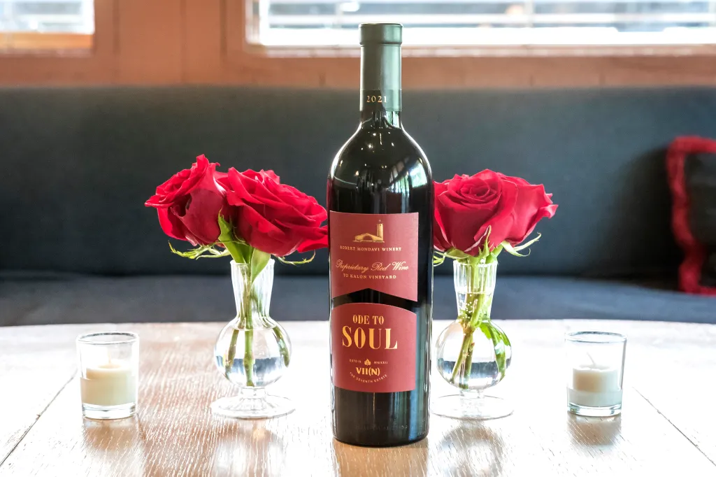 Robert Mondavi Winery "Ode to Soul" wine bottle next to red roses and candles.