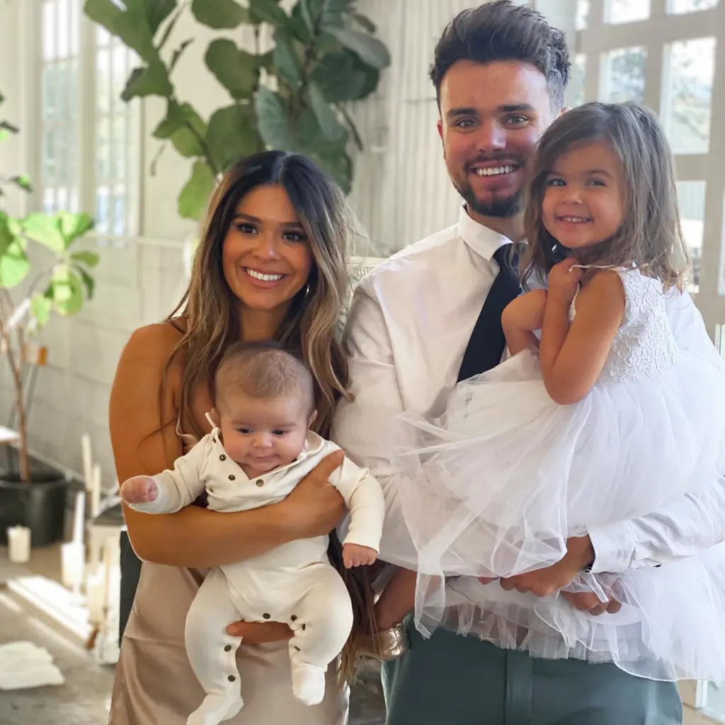 A smiling family of four: a woman holding an infant and a man holding a young girl.