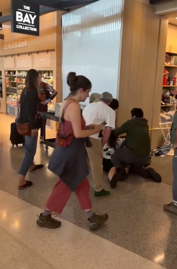 People gathered around a person on the floor in an airport.