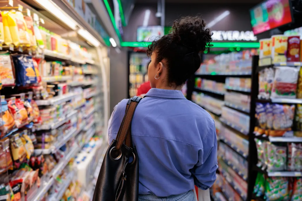 A woman with her back to the camera walks through a grocery store aisle filled with snacks.
