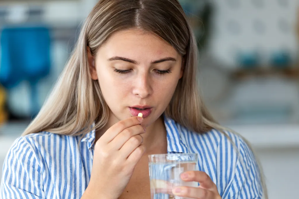 Young woman taking a yellow medicine pill with a glass of water.