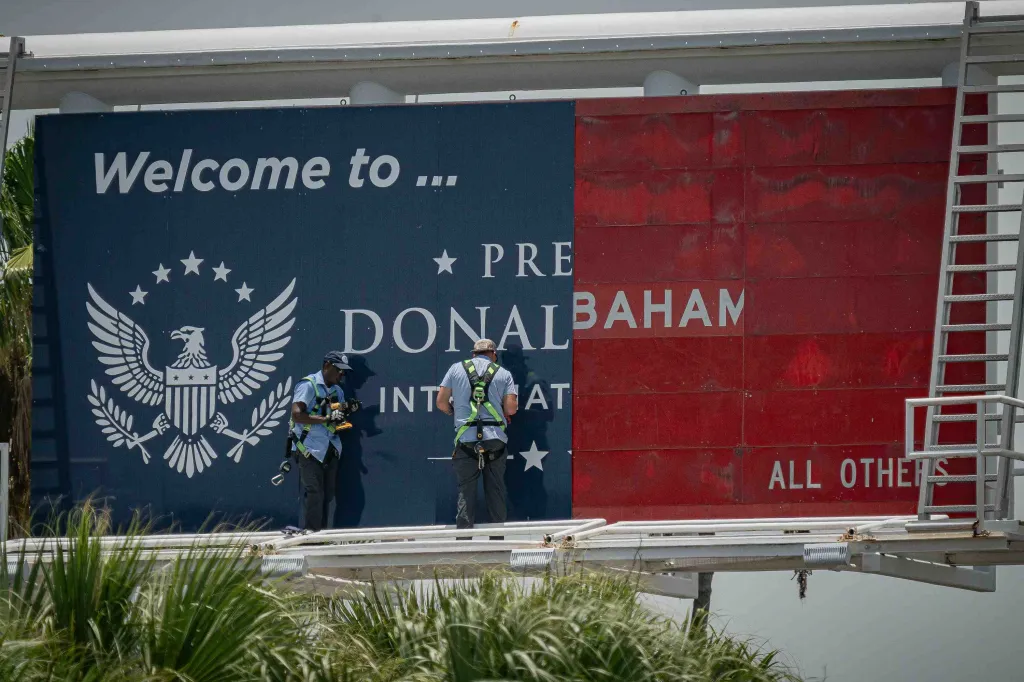 Two workers installing signage at Palm Beach International Airport, featuring a blue section with "Welcome to..." and an eagle seal, and a red section with text including "DONALBAHAN" and "ALL OTHERS".
