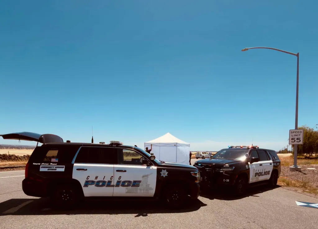 Two Chico Police vehicles parked on the side of a road with a white tent in the background.