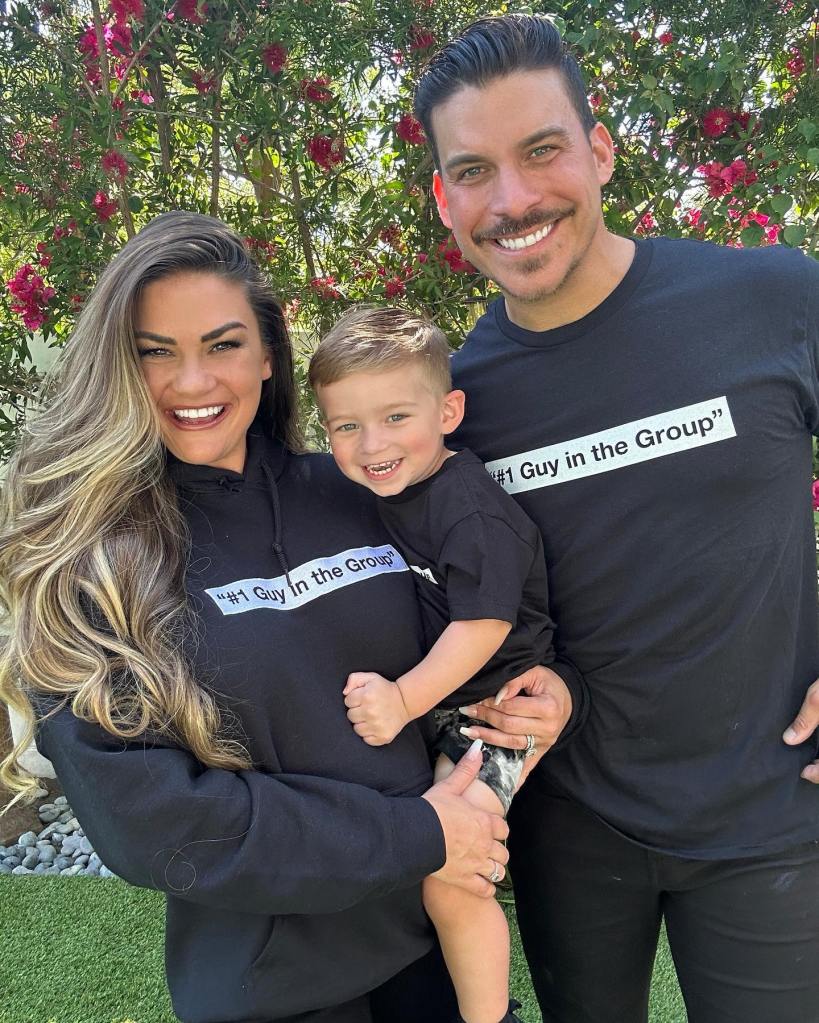 Brittany Cartwright and Jax Taylor holding their child, all wearing black shirts that say "#1 Guy in the Group".