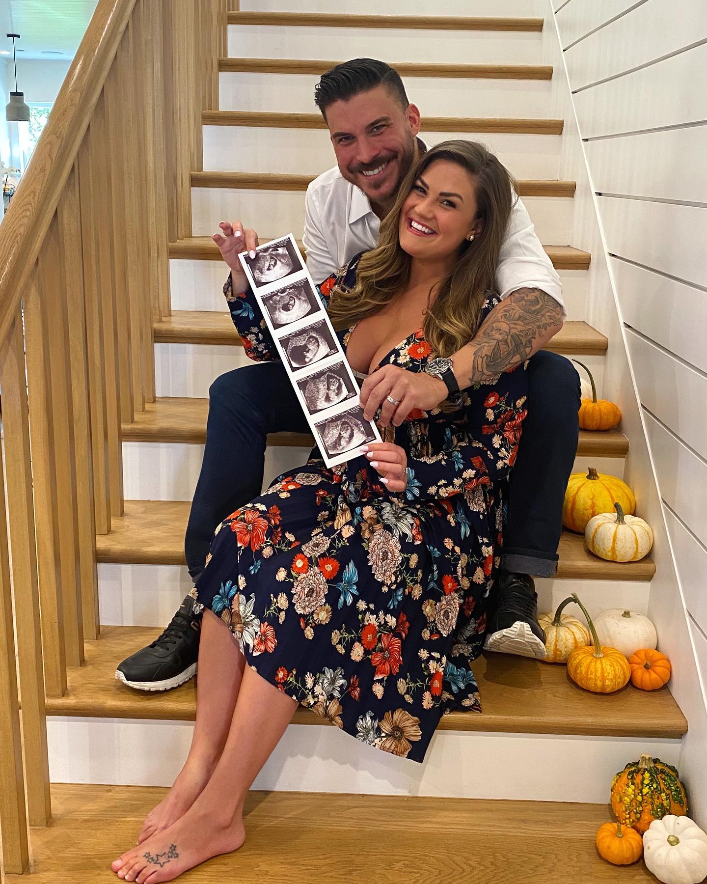 Jax Taylor and Brittany Cartwright seated on stairs, holding up a strip of sonogram images.