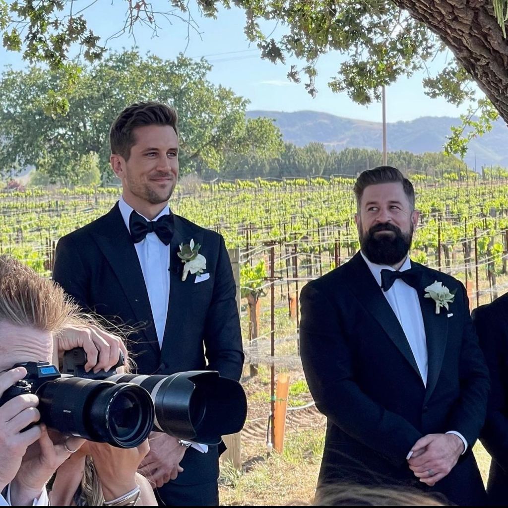 Jordan Rodgers and Luke Rodgers dressed in tuxedos, standing at an outdoor event in a vineyard.