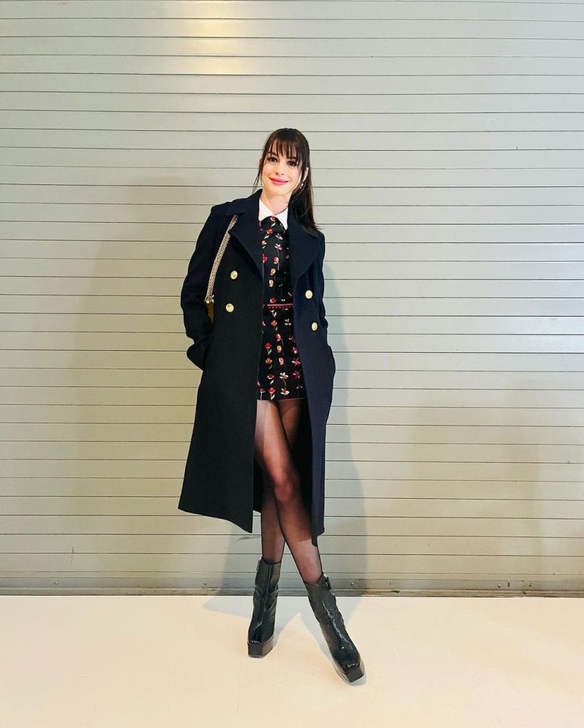 Anne Hathaway wearing a dark coat over a floral dress.