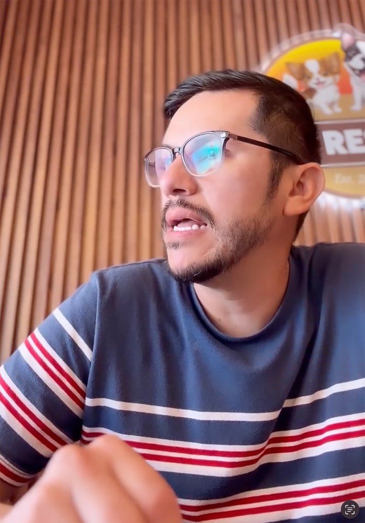 A man with glasses and a beard, wearing a striped shirt, looks to his right while talking.