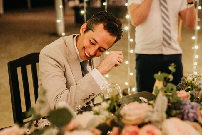 Josh Grisetti laughing while sitting at a table with a glass of red wine.