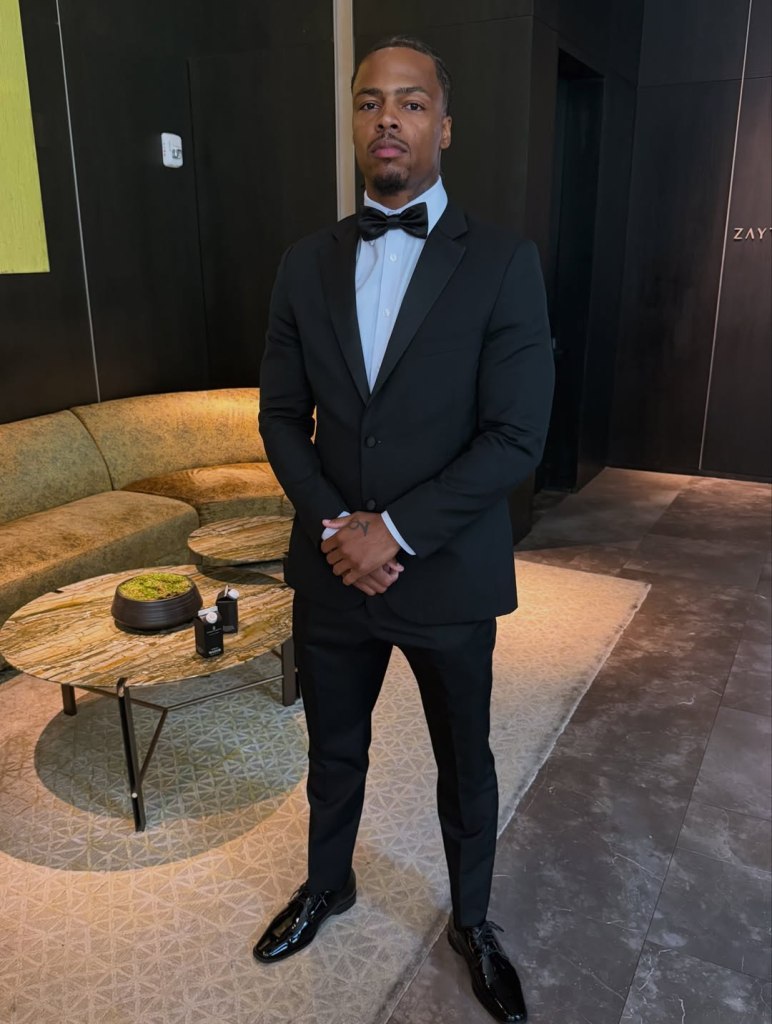 A man in a tuxedo stands in a room with a lounge area.