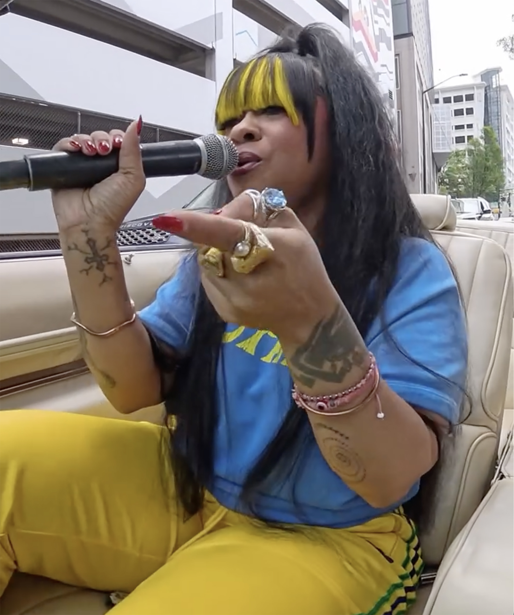 Singer Nivea with yellow bangs, wearing a blue shirt and yellow pants, holding a microphone.