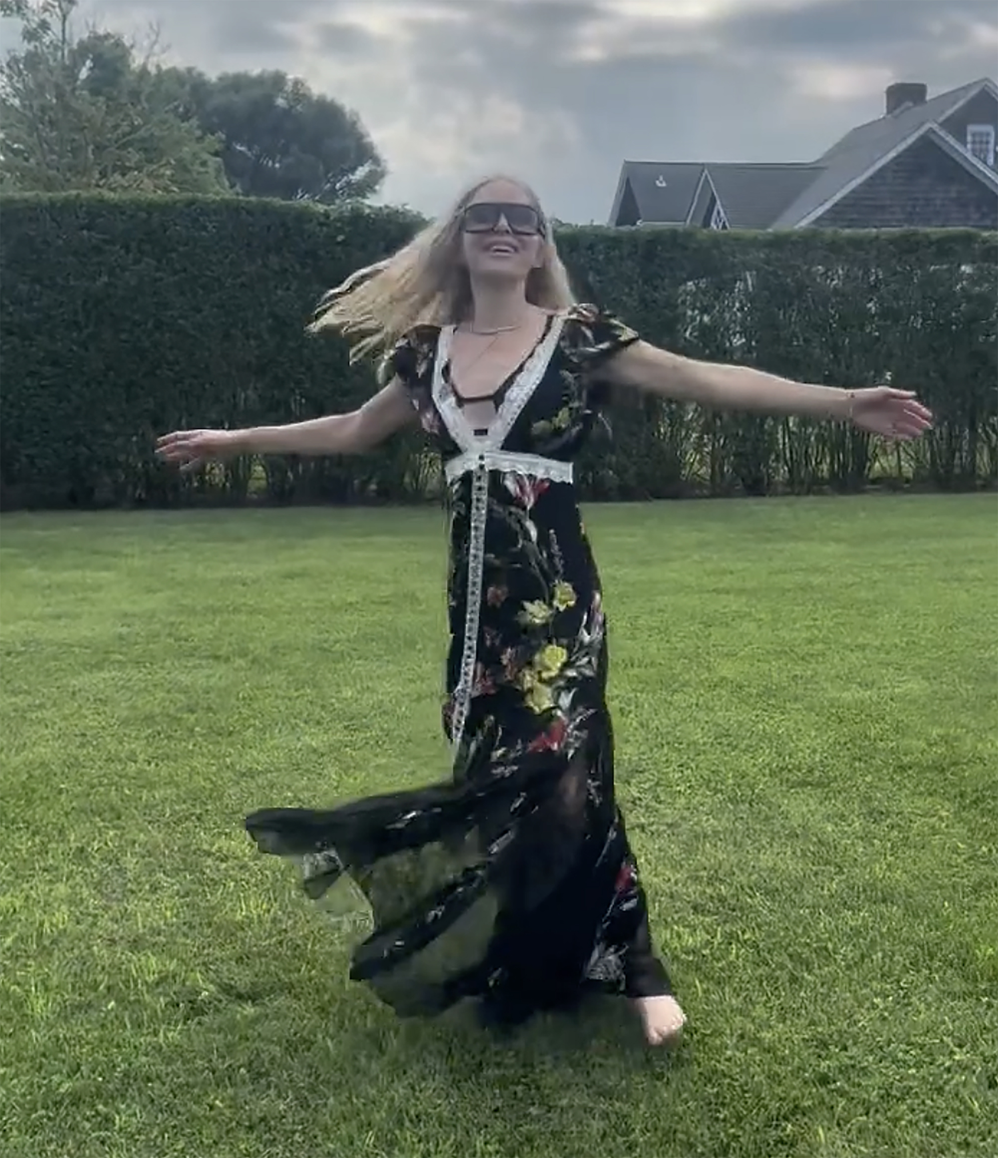 Jenny Mollen twirling in a black floral dress on a grassy lawn.
