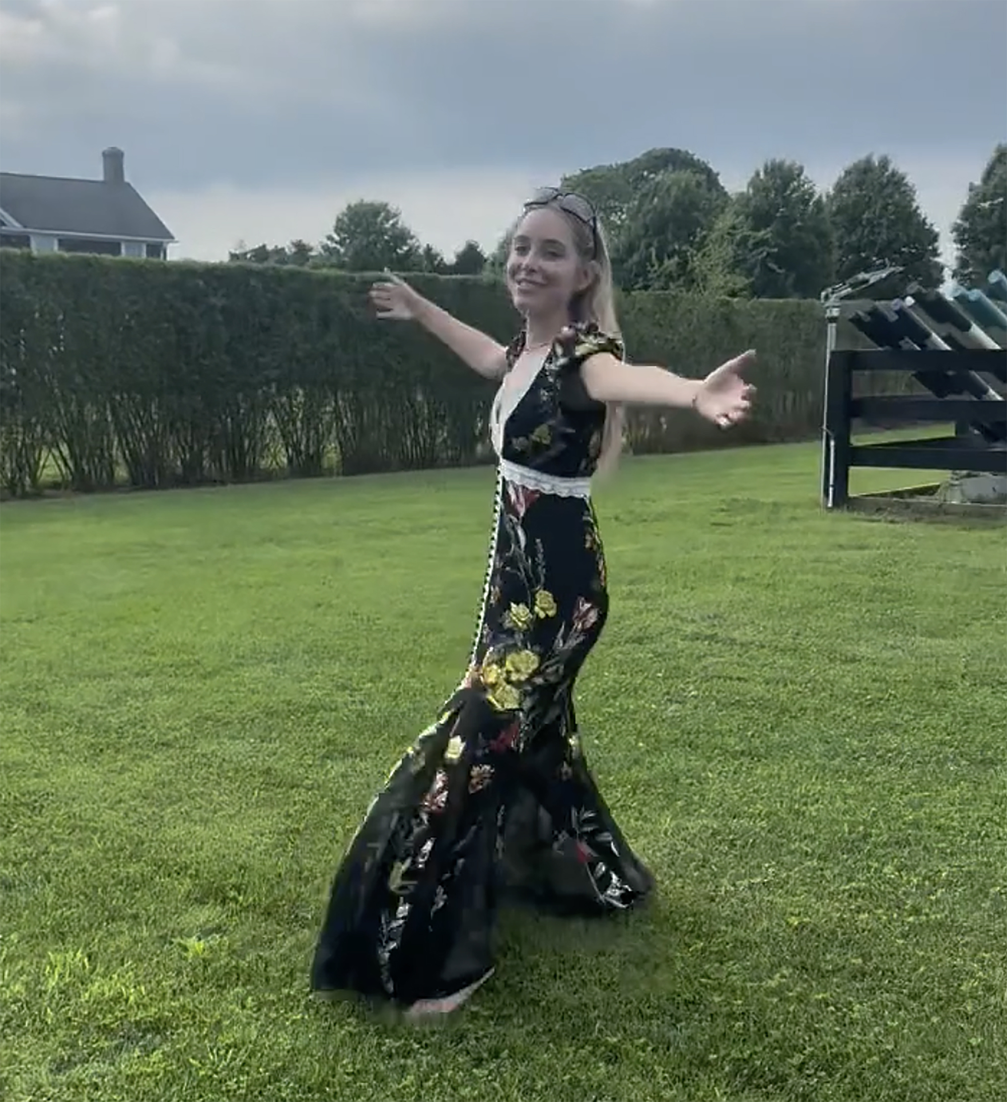 Jenny Mollen twirling in a black floral dress on a grassy lawn.