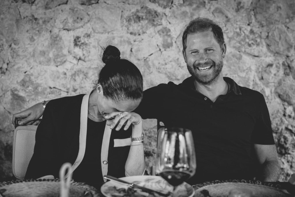 Meghan Markle laughing while sitting next to a smiling Prince Harry.