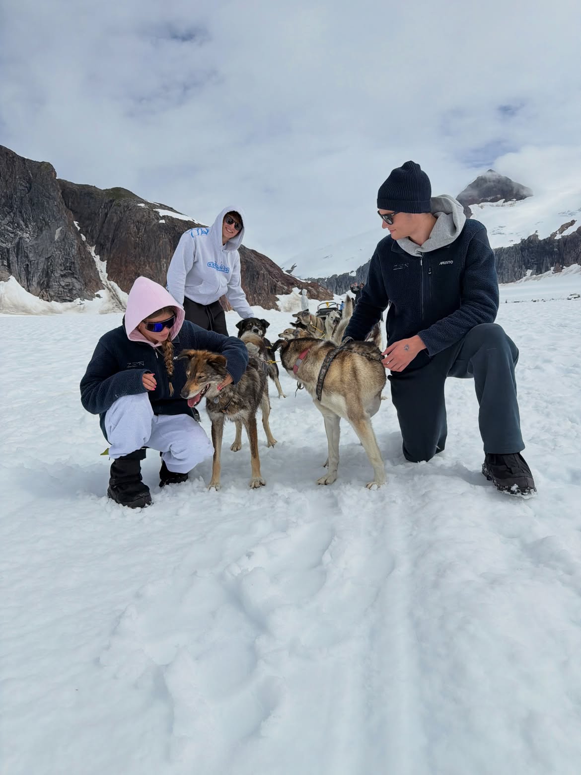 Vivian Brady petting sled dogs in the snow, with mountains in the background.