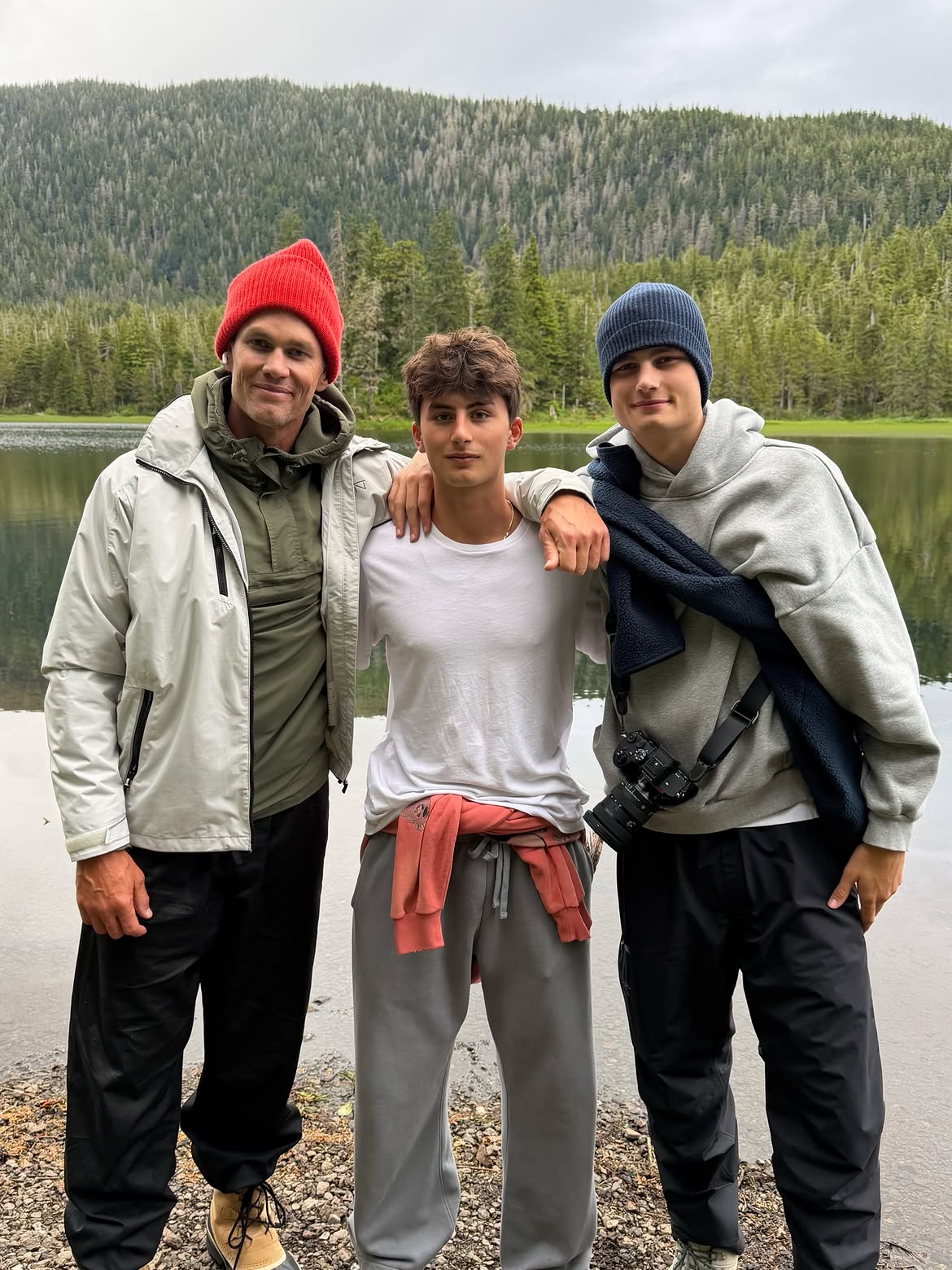 Tom Brady with his two sons by a lake, surrounded by a pine forest.