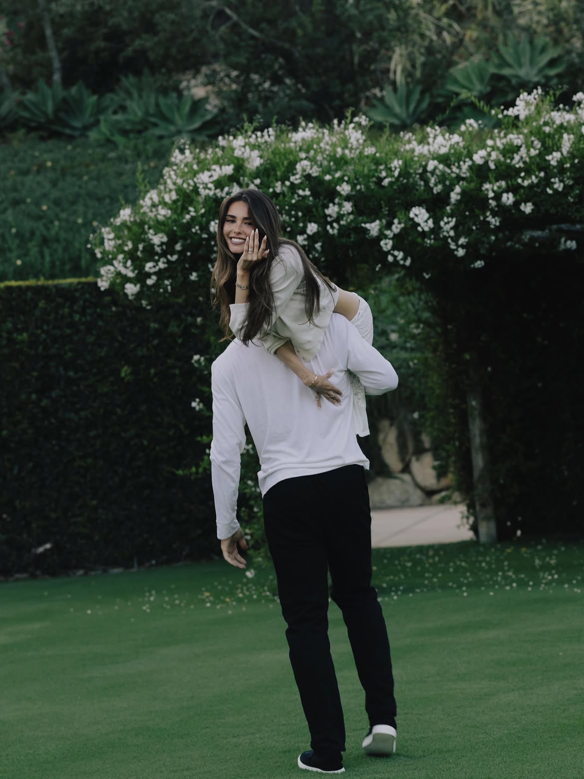 Madison Beer being carried piggyback by Justin Herbert, smiling and showing off an engagement ring.
