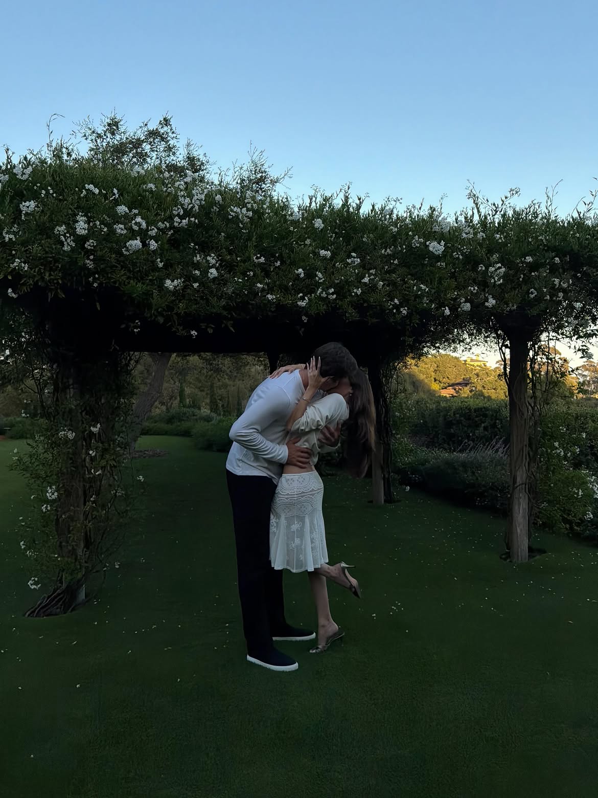 Madison Beer and Justin Herbert kissing under a flowering archway.
