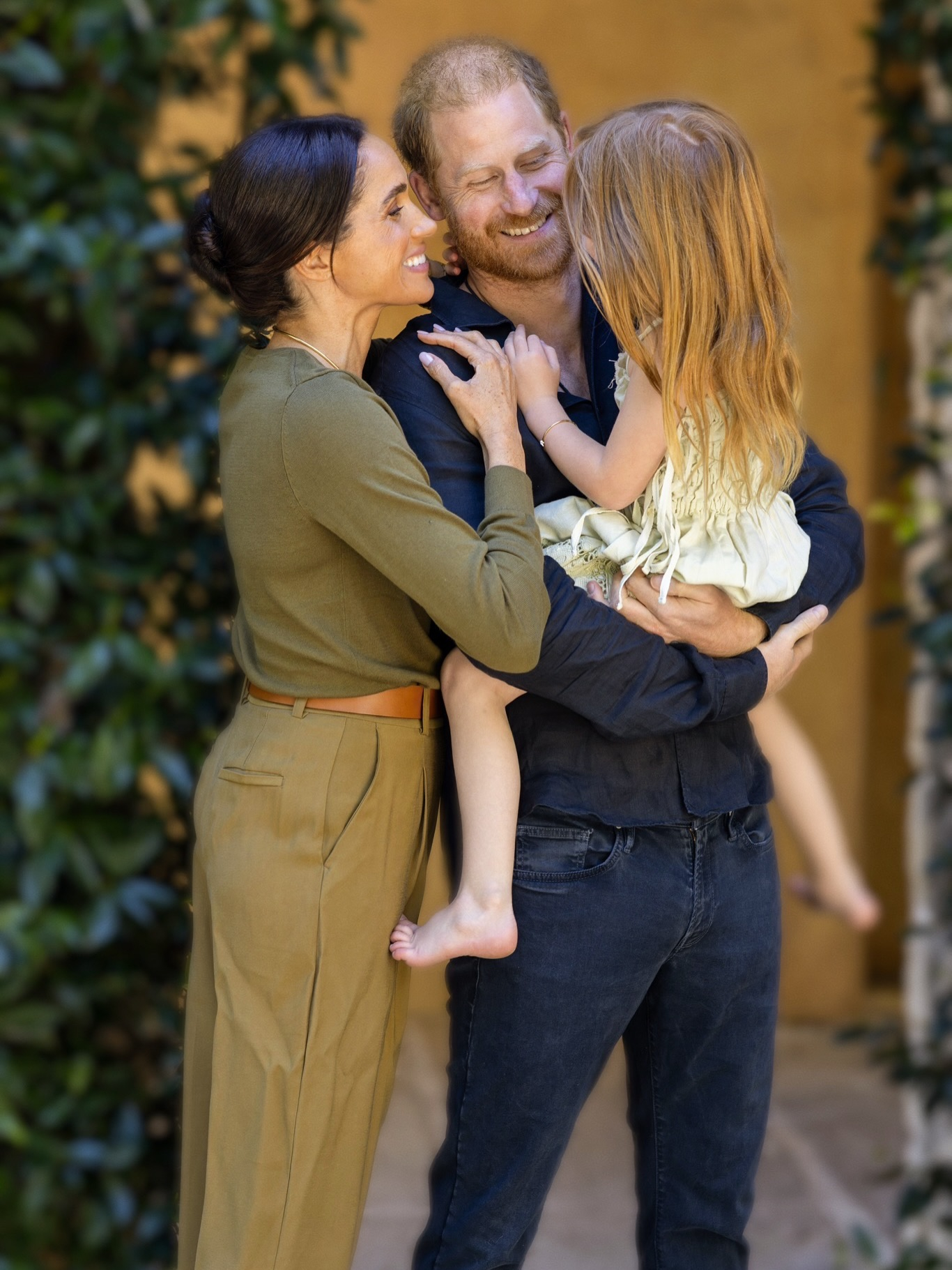 Meghan Markle and Prince Harry smiling with their daughter.