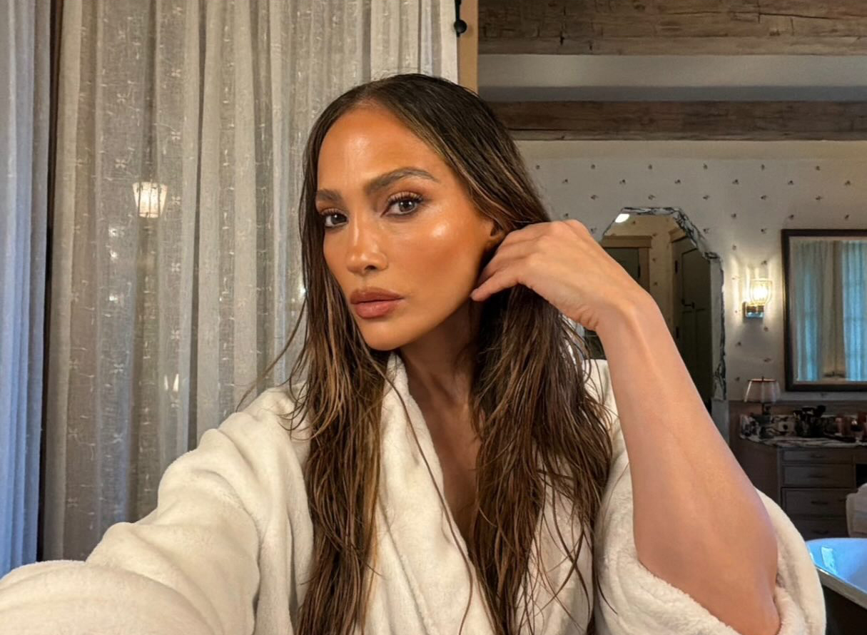 Jennifer Lopez in a white robe with wet hair, with glowing skin and makeup.