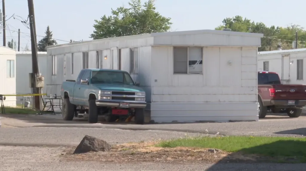 A green pickup truck parked outside a white trailer home in a trailer park.