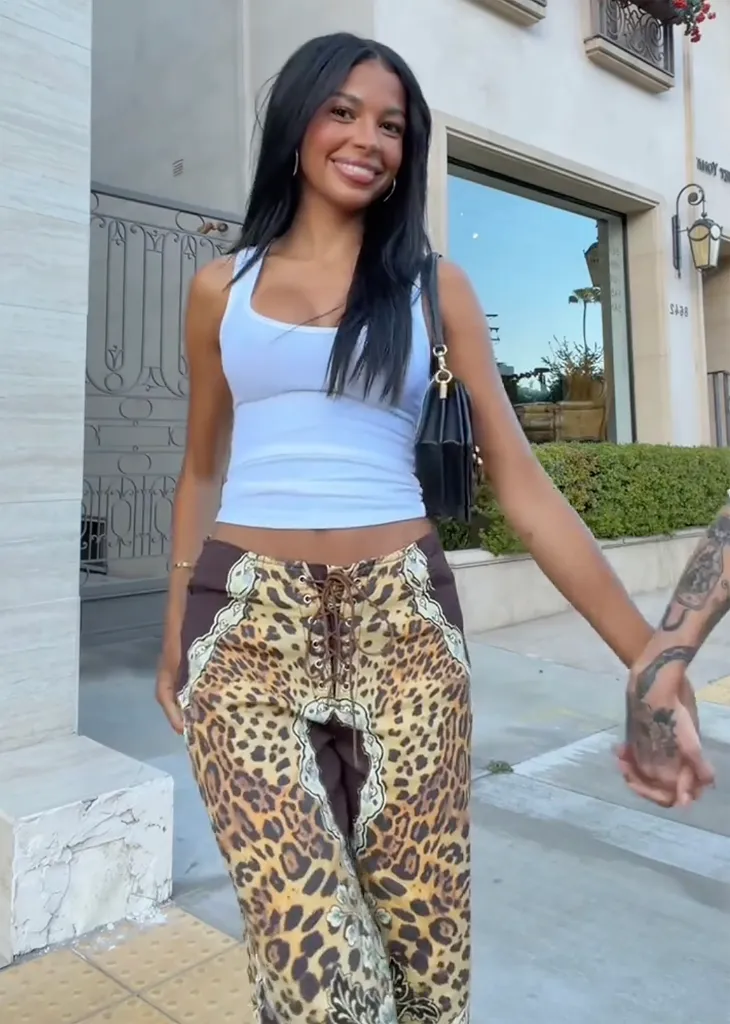 Layla Taylor in a white tank top and leopard print pants, holding hands with a tattooed person.