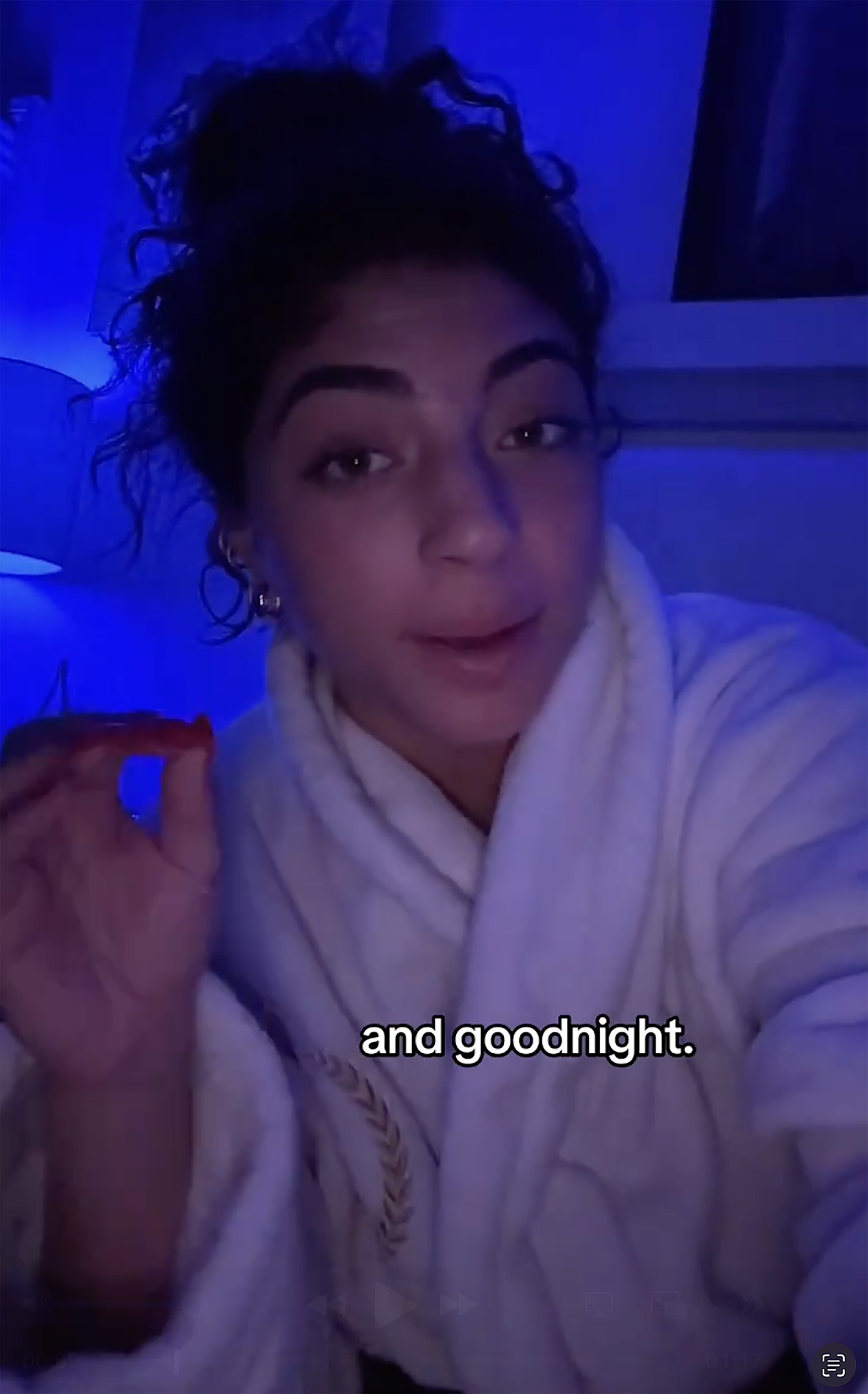 A woman with dark, curly hair in a bathrobe holding a red gummy candy.
