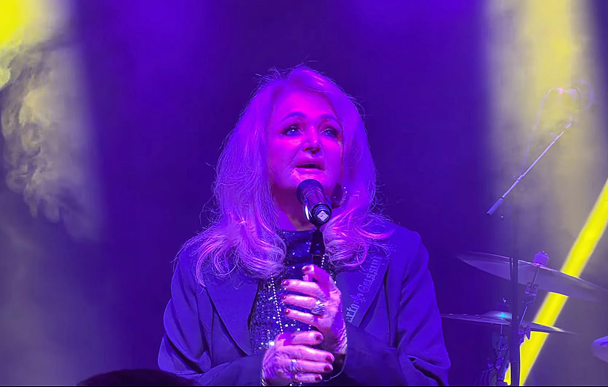 Bonnie Tyler performing on stage, lit by purple and yellow lights.