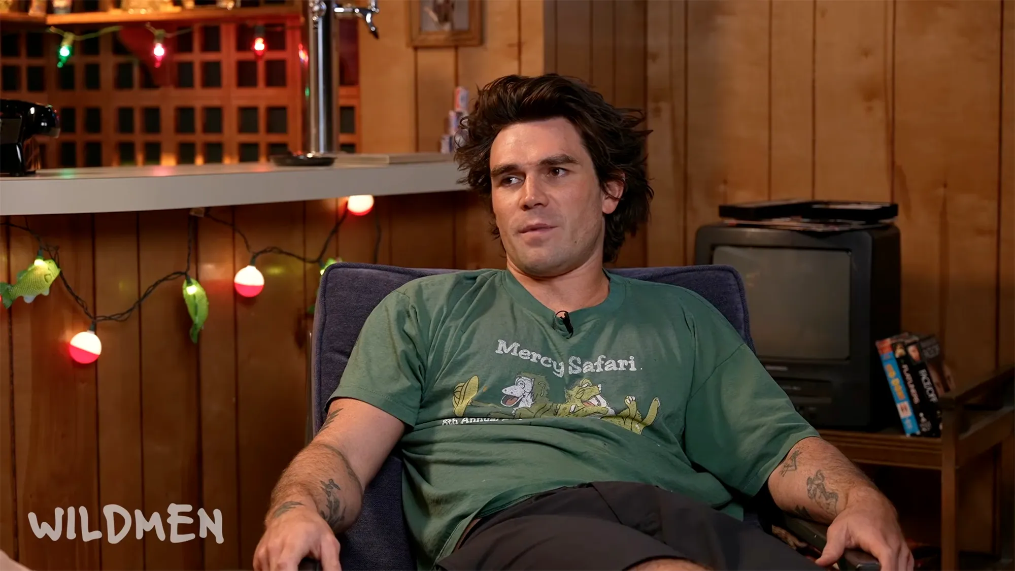 KJ Apa sitting on a dark blue chair while being interviewed on the Wildmen podcast.