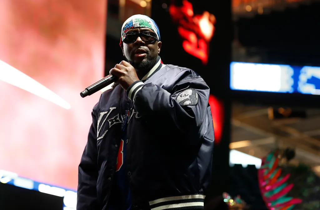 Wyclef Jean performing on stage, holding a microphone.