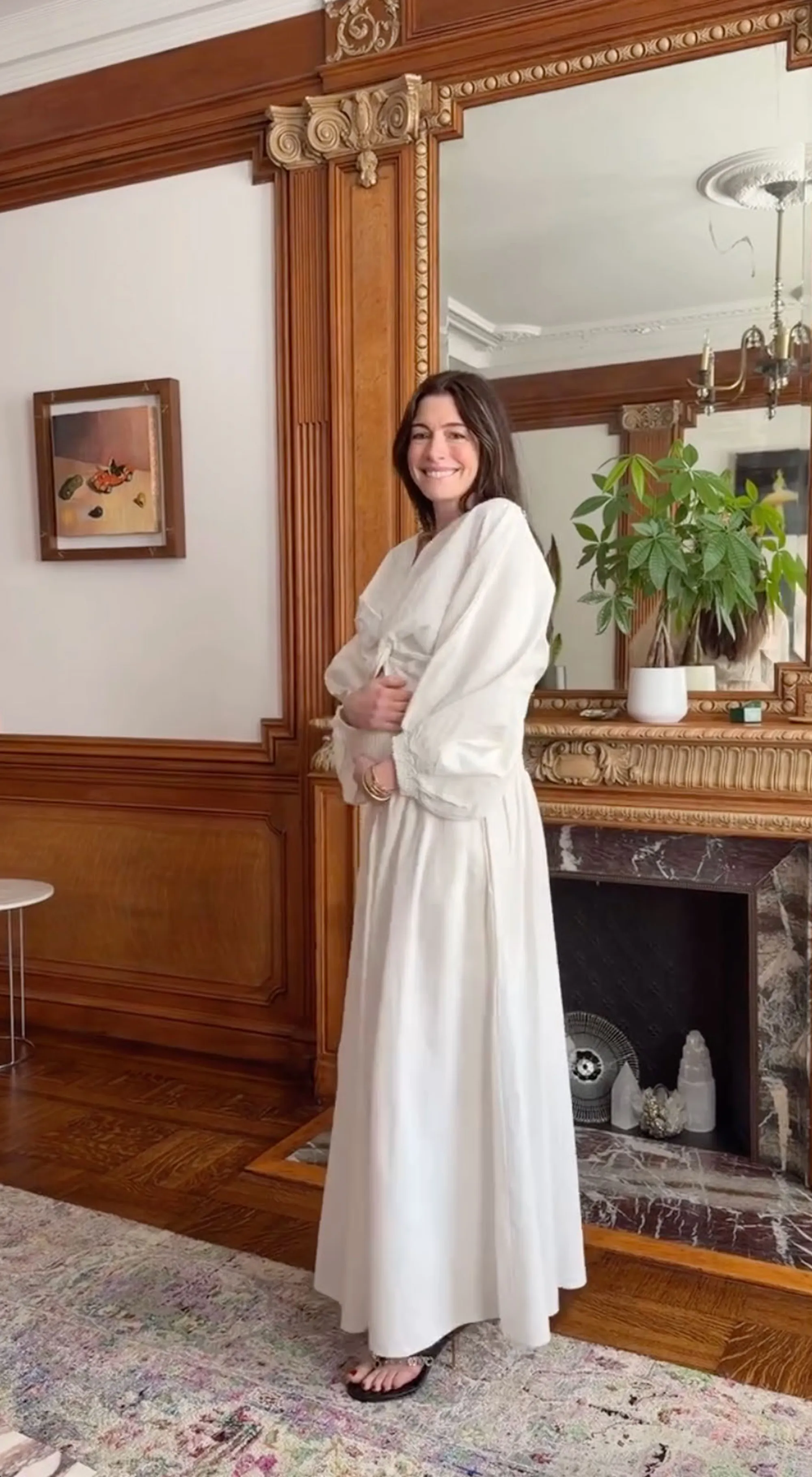 Anne Hathaway smiling in a white dress inside a grand room.