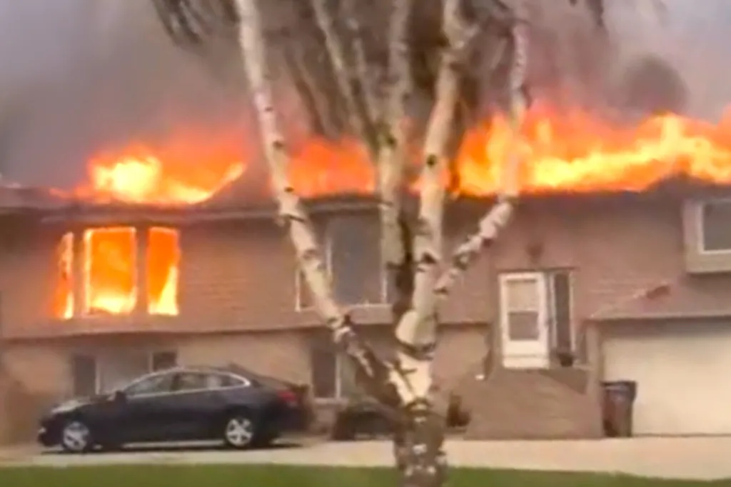 A house engulfed in flames, with thick smoke rising from the roof and bright orange fires visible through the windows.